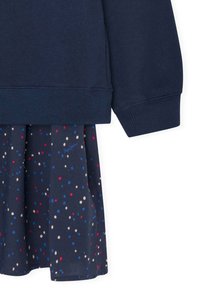 Sudadera azul marino con puños acanalados, combinada con una falda azul marino que presenta un patrón de lunares multicolores en rojo, azul y crema.