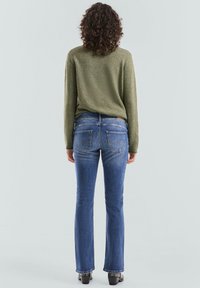 Groene textuurtrui gecombineerd met donkerblauwe flared jeans. De jeans hebben twee achterzakken met subtiele stikaccenten.