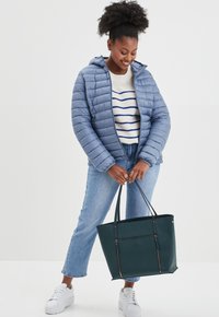 Lichtblauwe pufferjack met horizontale stiksels, witte gebreide trui met blauwe strepen, blauwe spijkerbroek en een donkergroene schoudertas. Witte sneakers.