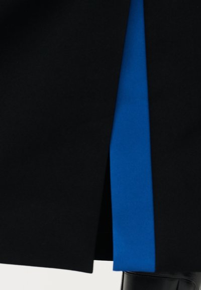 Peça preta com um painel azul de destaque. O tecido parece liso, apresentando uma fenda lateral que revela o azul por baixo.