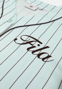 Light blue jersey with thin vertical brown stripes, "Fila" logo in cursive brown on front, and brown piping along the collar.