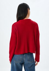 Rot gestreifter Pullover mit lockerer Passform, überschnittenen Schultern und cropped Saum. Kombiniert mit blauen, hochtaillierten Jeans aus Denim mit Gesäßtaschen.