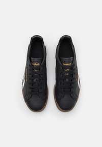 Svarta lädersneakers med vita detaljer, med en texturerad yta, rundad tå och brun gummisula. Guldlogotypdetalj på sidan.