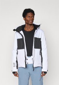 Ανδρικό μπουφάν με σχέδιο σε λευκό και μαύρο χρώμα, με φερμουάρ στις τσέπες, κουκούλα και κομψή υφή υφάσματος.