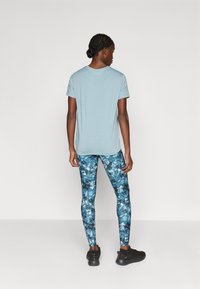 Gaiši zils T-krekls ar īsām piedurknēm, kas apvienots ar krāsainām ziedu raksta legingām zilās un melnās nokrāsās, papildināts ar melniem sporta apaviem.