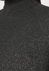 Gros plan sur un tissu côtelé à col roulé noir pailleté avec une texture subtilement scintillante.