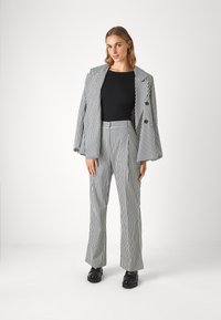 Gestreifter Anzug in Schwarz und Weiß mit einem taillierten Blazer mit weiten Ärmeln und ausgestellten Hosen, kombiniert mit einem enganliegenden schwarzen Top und klobigen Schuhen.