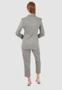 Completo grigio a righe sottili con giacca aderente e pantaloni cropped, realizzato in un tessuto liscio. Presenta un revers a scollo a V e un design slim fit.