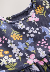 Blommig klänning med marinblå bakgrund och färgglada blommor i rosa, gult och blått, texturerat tyg och rund halsringning.