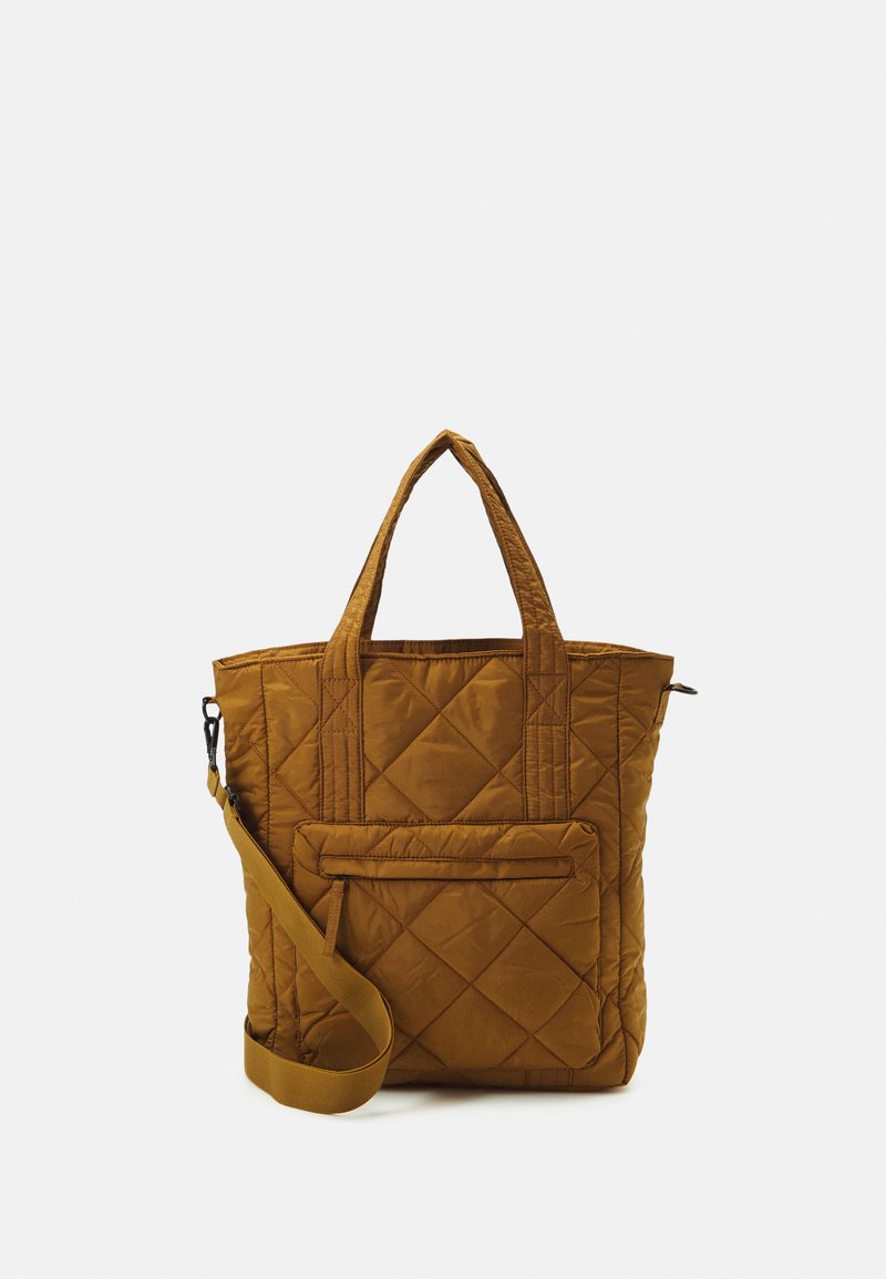 Sacola tote acolchoada em amarelo mostarda com alças duplas, alça de ombro ajustável e bolso frontal com zíper. Textura suave e forma retangular.