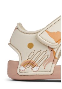 Beige sandal with velcro strap, featuring pastel graphic patterns of a sun, unicorn, and rainbow on a textured, rubber sole.