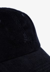 Gorra de pana negra con una superficie texturizada, que presenta un bordado sutil de calavera y huesos cruzados en la parte frontal.