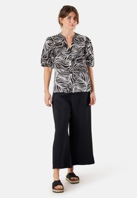 Zwart-wit geblokte blouse met pofmouwen, met knoopsluiting aan de voorkant; gecombineerd met losse zwarte broek en zwarte sandalen met een natuurlijke zool.
