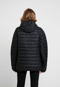 Doudoune noire à capuche avec un motif matelassé, offrant une coupe décontractée et un tissu durable. Surface texturée avec une finition lisse.