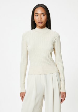 Pull à col montant en ribbed crème avec des manches longues et une coupe ajustée, fabriqué à partir d'un matériau doux et extensible.