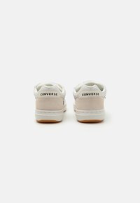 White and beige suede sneakers with a smooth texture, featuring a rubber sole and "CONVERSE" logo on the heel. Low-top design.