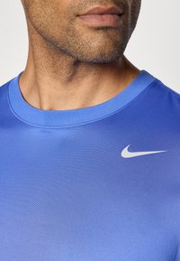 Blå kortærmet sports T-shirt lavet af syntetisk stof; har en rund halsudskæring og et lille hvidt Nike swoosh-logo på brystet.
