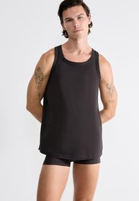 Débardeur noir sans manches en matériau doux et lisse, avec un col rond et une coupe décontractée, associé à un short assorti de couleur foncée.