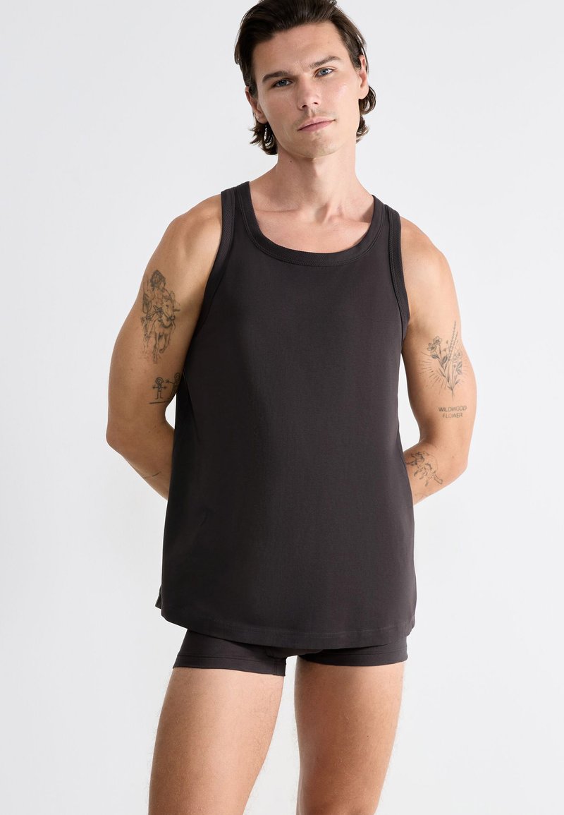 Débardeur noir sans manches en matériau doux et lisse, avec un col rond et une coupe décontractée, associé à un short assorti de couleur foncée.