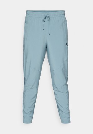 Light blue athletic pants with elastic waistband, drawstring, tapered fit, side pockets, and a black logo on the left thigh.