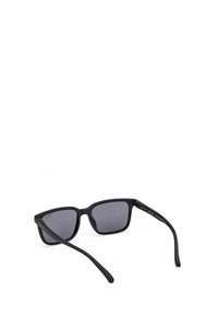 Gafas de sol de plástico negro con lentes gris tintados. Forma cuadrada con un acabado mate y varillas delgadas. Presenta el logo de la marca en el lateral.