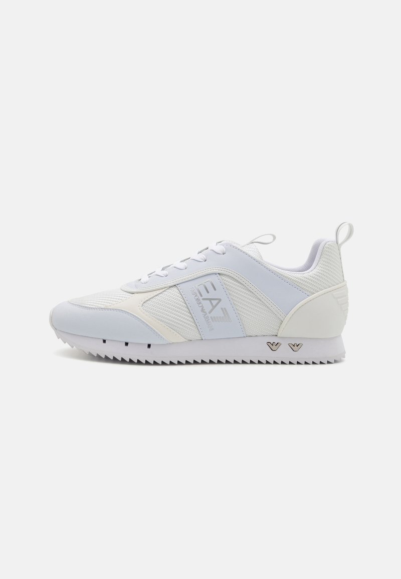 Weißer Sportschuh mit einer Mischung aus glatten und Mesh-Oberflächen, elegantem Design und gezackter Außensohle. Branding an der Seite sichtbar.