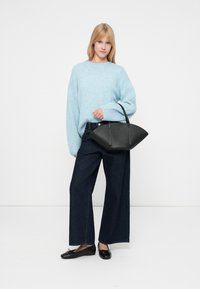 Jasnoniebieski, oversize sweter z dzianiny; szerokie, ciemne dżinsy; czarne baleriny; czarna torba z zaokrąglonymi krawędziami i minimalnymi detalami.