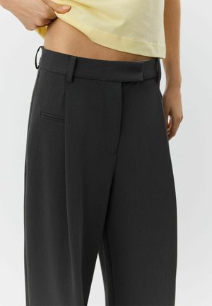 Pelēkas augsta jostas bikses ar krokotu priekšpusi, sānu kabatām un auduma jostas cilpām. Materiāls šķiet gluds ar izstrādātu dizainu.