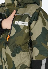Camouflagejack in groen en beige, met een fleece-voering in de capuchon, elastische manchetten, ritszakken en een opvallende logo-opdruk.