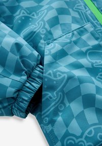 Manche de veste bleu clair et poche avec poignet élastique et motifs de chiens en contour sur un tissu à carreaux.