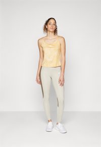 Débardeur jaune tie-dye à bretelles étroites associé à un legging gris clair avec un panneau latéral gris plus foncé. Chaussures de sport blanches.