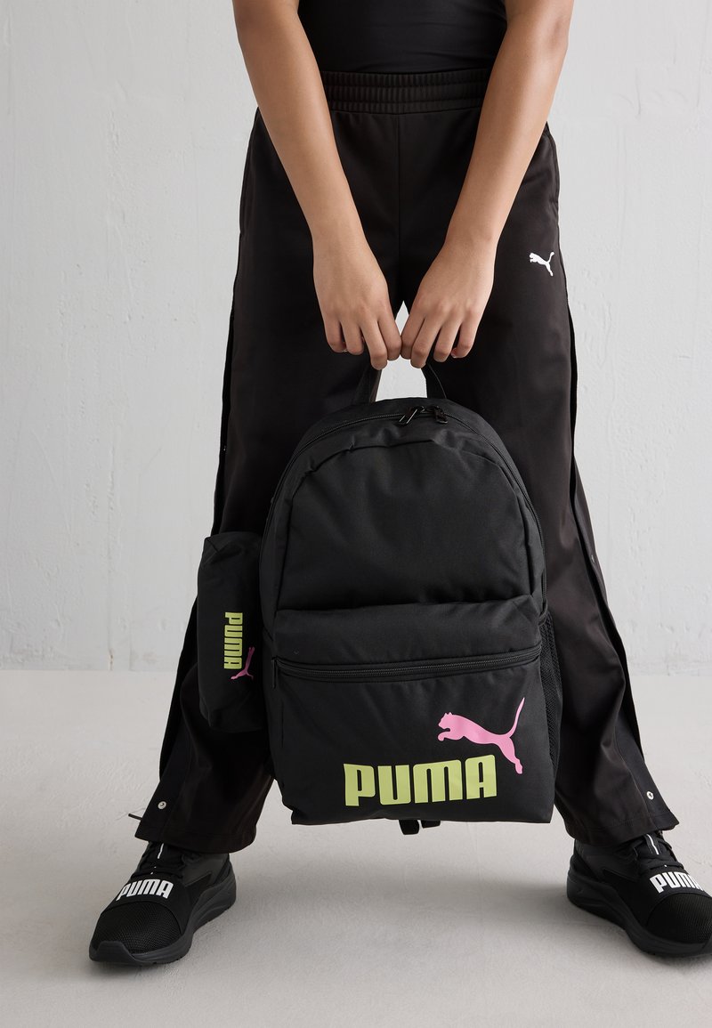 Juodas kuprinės su rožiniu Puma logotipu, turinti priekinį kišenę ir reguliuojamus diržus. Dėžutėje taip pat yra juodas pamušalinys su virvute.