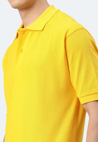 Gelbes Polohemd aus strukturiertem Stoff, mit einem klassischen Kragen, kurzen Ärmeln und einer Knopfleiste auf der Vorderseite.