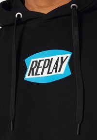 Sudadera negra con cordones negros y un logo azul y blanco de "REPLAY" impreso en el pecho.
