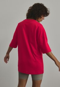T-shirt oversize a maniche corte in cotone rosa brillante, caratterizzato da un fit rilassato e un colletto rotondo, abbinato a pantaloni corti grigi a coste.