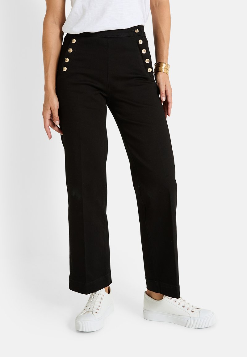 Pantalones negros de cintura alta con frente plano, detalles de botones dorados en los lados y un diseño de pierna recta. Combinados con zapatillas blancas.