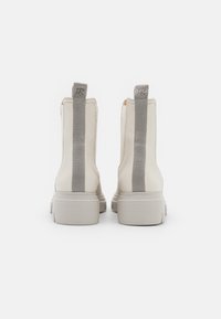 Botas de tobillo blancas hechas de cuero suave con acentos de textil gris, que presentan una suela gruesa estriada y tiras en la parte posterior.