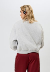 Pelēks pārmērīgs krekliņš ar ribotas apkakles un piedurknēm, apvienots ar burgundijas biksēm, kurām ir baltas sānu svītras. Melni austiņas uz galvas.