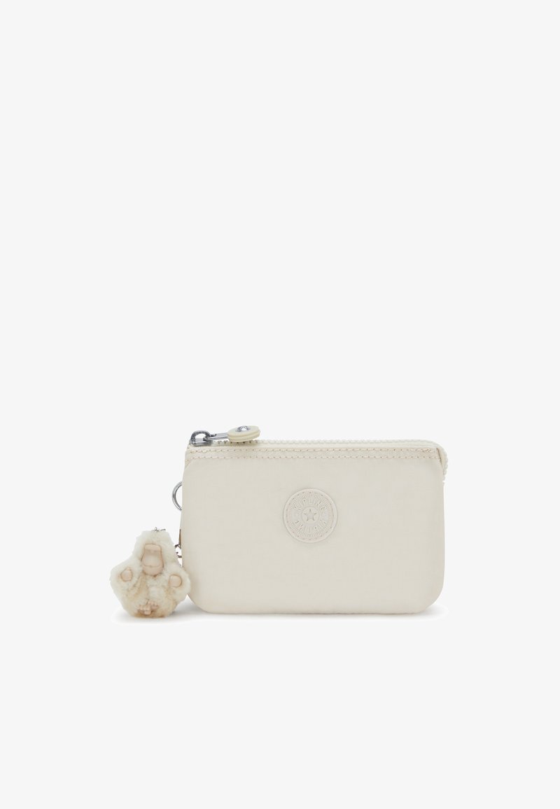 Zip peněženka v krémové látce s embosovaným logem, obsahující plyšový přívěsek. Kompaktní obdélníkový tvar se šitými detaily.