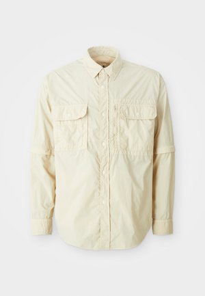 Chemise à manches longues beige clair en tissu léger, avec deux poches poitrine et des manches retroussées. Design à boutons avec un col pointu.