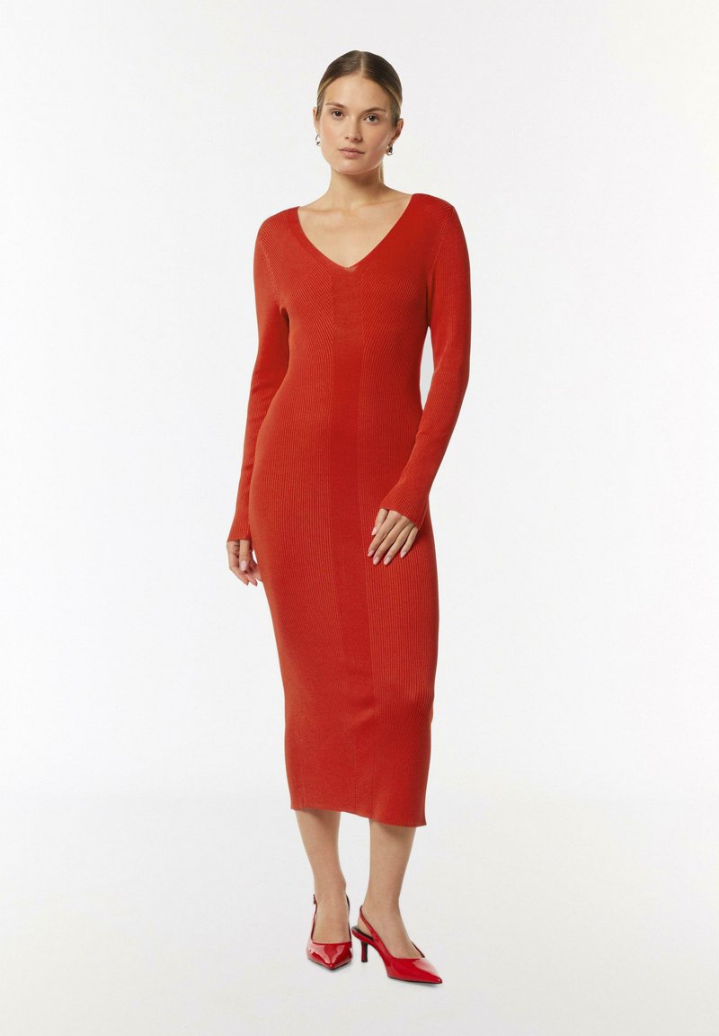 Langärmliges Midikleid aus geripptem Strickstoff, leuchtend rote Farbe, V-Ausschnitt-Design, figurbetonte Form, kombiniert mit roten High Heels.