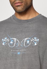 T-shirt de algodão cinza com um design gráfico de três dados com detalhes em azul e o texto "HISTORY MAKERS" acima de um retângulo azul rotulado "CITY."