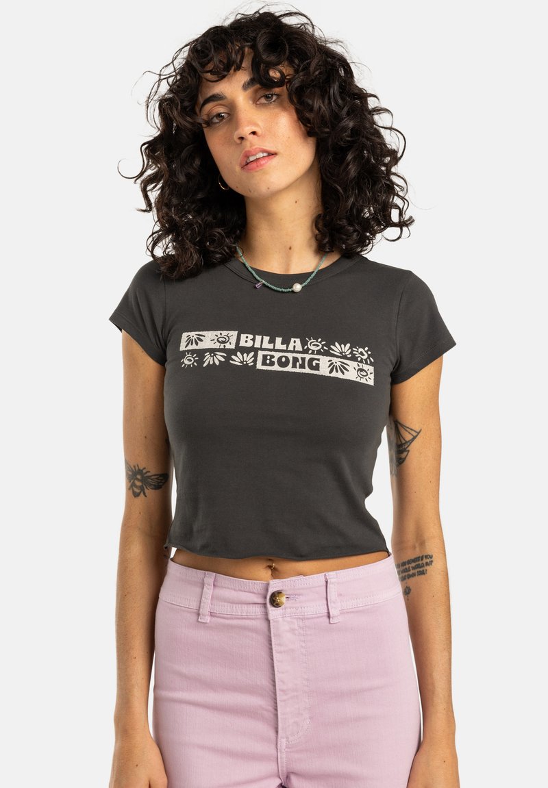 Svart avkortet t-skjorte med hvit "BILLA BONG" logo og dekorative mønstre. Modellen har også på seg lyse rosa høyt_skåret jeans.