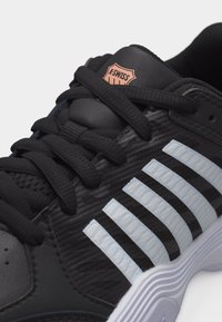 Κοντινό πλάνο ενός μαύρου αθλητικού παπουτσιού K-Swiss με μαύρα κορδόνια, λευκές ραβδώσεις στο πλάι με υφή και υφή στη λευκή σόλα.