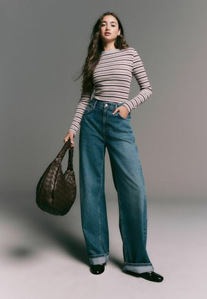 Maglietta a maniche lunghe a righe in grigio, rosa e blu; jeans a vita alta blu in denim a gamba larga; borsa intrecciata marrone; scarpe nere.