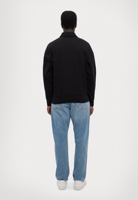 Svart oversized sweatshirt med ribbad fåll, buren med ljusblå raka jeans och vita sneakers, sedd bakifrån.