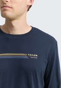 Marineblauwe longsleeve t-shirt van zachte katoen, met een horizontaal streepdesign in geel, blauw en rood met de merknaam "TOM TAILOR."