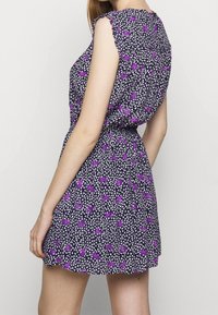 Lyhythihainen mekko tummansinisellä pohjalla, jossa on toistuva violetti ja valkoinen kukkakuosi, kootut vyötärö ja liehuva helma. Pehmeä kankaan rakenne.