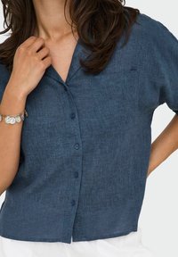 Camicia a maniche corte di colore blu scuro, con tessuto in misto lino e una piccola tasca sul petto. Presenta una vestibilità rilassata e un colletto.