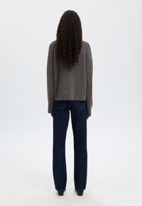 Szary sweter dzianinowy o luźnym kroju, zestawiony z ciemnoniebieskimi dżinsami o prostym kroju. Na plecach widoczne kręcone włosy. Gładka tekstura.